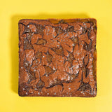 Salted Caramel Brownie by Crumbs & Doilies with fudgy base, crispy top, swirls of caramel, and sea salt flakes on yellow background.